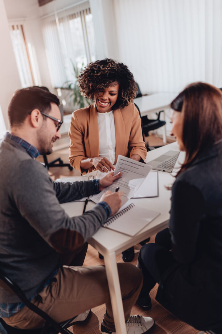 Three colleagues collaborate at a desk with documents and a laptop.