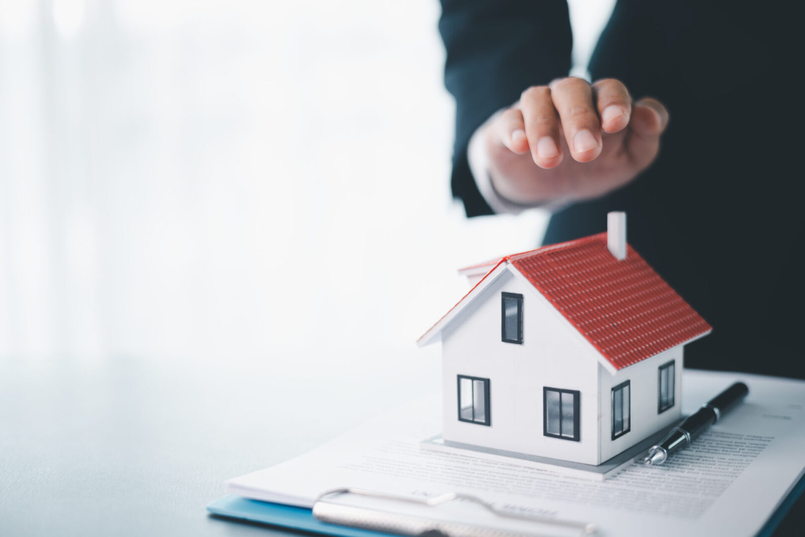 A person holding a small house model, symbolizing real estate or home ownership.